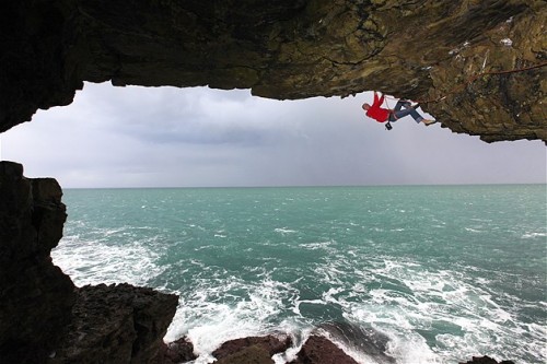 Un escalador trepa por una cueva en el mar cerca de Swanage, Dorset.